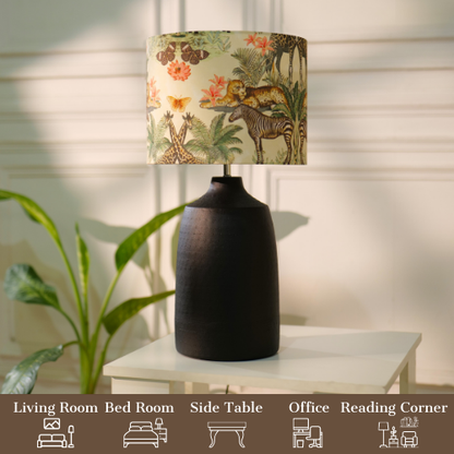 Table lamp with a dark, textured metal base and a floral-patterned fabric shade, placed on a white table in a room with plants