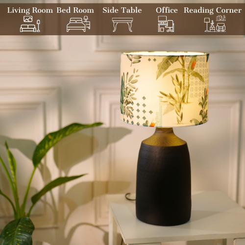 Table lamp with a dark, textured metal base and a floral-patterned fabric shade, placed on a white table in a room with plants