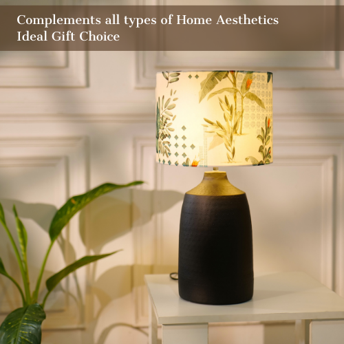 Table lamp with a dark, textured metal base and a floral-patterned fabric shade, placed on a white table in a room with plants