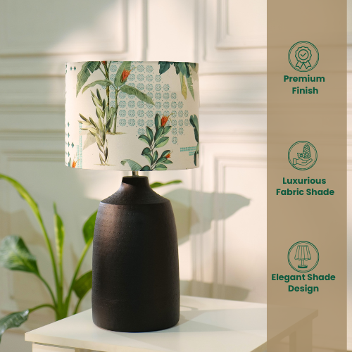 Table lamp with a dark, textured metal base and a floral-patterned fabric shade, placed on a white table in a room with plants