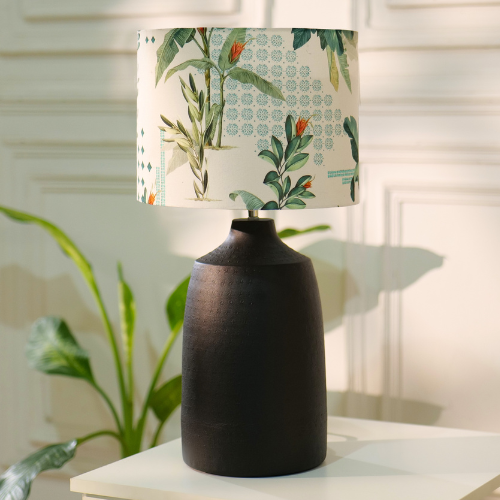 Table lamp with a dark, textured metal base and a floral-patterned fabric shade, placed on a white table in a room with plants