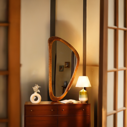 Wooden-framed asymmetrical mirror above a wooden dresser, styled with a white vase and a lamp