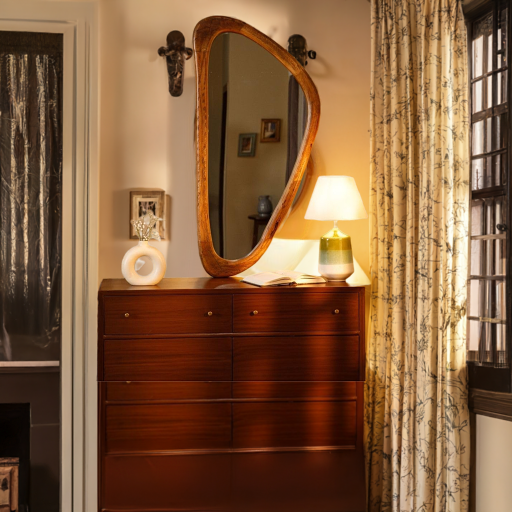 Wooden-framed asymmetrical mirror above a wooden dresser, styled with a white vase and a lamp